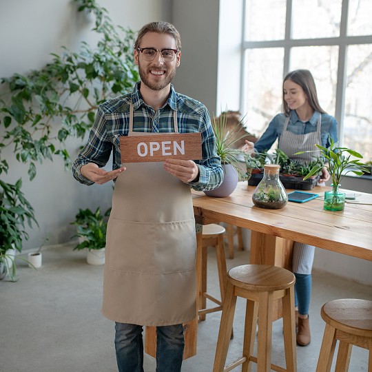 Small business owner holding an open sign with co worker in the back